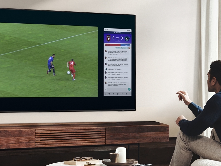 A man is using QLED's Multi view feature to enjoy a football match and view news on the same screen at the same time.