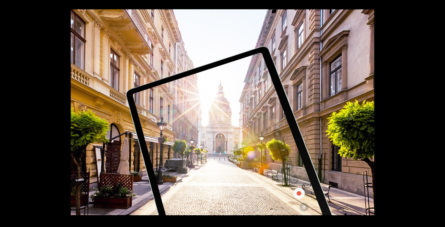 Tablet Samsung Galaxy Tab S9 FE w trybie nagrywania. Na ekranie widzimy ulicę z klasyczną europejską zabudową oraz flarę słońca padającego wprost w obiektyw. W tle przestrzeń miejska, która dopełnia widok wyświetlany na urządzeniu.